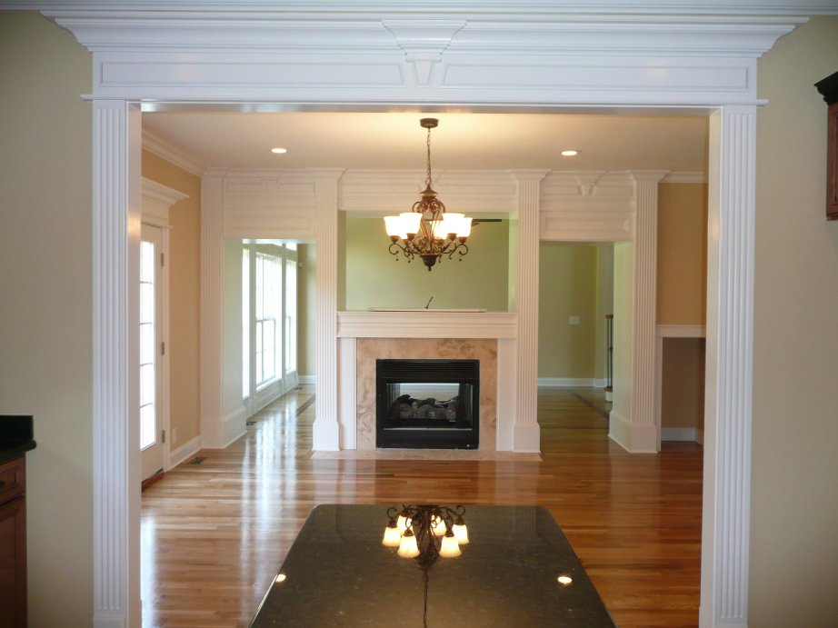 View through a wide white-trimmed doorway into a room with a fireplace, chandelier, and hardwood floors.