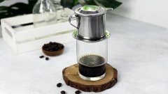 Dùng nước sôi tráng qua phin pha cafe để đảm bảo phin được sạch, bên cạnh đó phin cafe ấm sẽ giúp cafe nở đều hơn và giảm bớt sự hấp thu nhiệt khi pha cà phê. Cho vào phin 3 muỗng bột cafe (khoảng 25gr) lắc đều. Đặt phin lên cốc tiến hành rót chậm và đều khắp bề mặt phin khoảng 50ml nước sôi cho cafe nở đều. Nước cafe sẽ bắt đầu nhỏ từng giọt xuống ly, đợi đến khi cafe nhỏ gần hết bạn ấn chặt nắp gài để chiết xuất hết lượng cà phê còn lại.