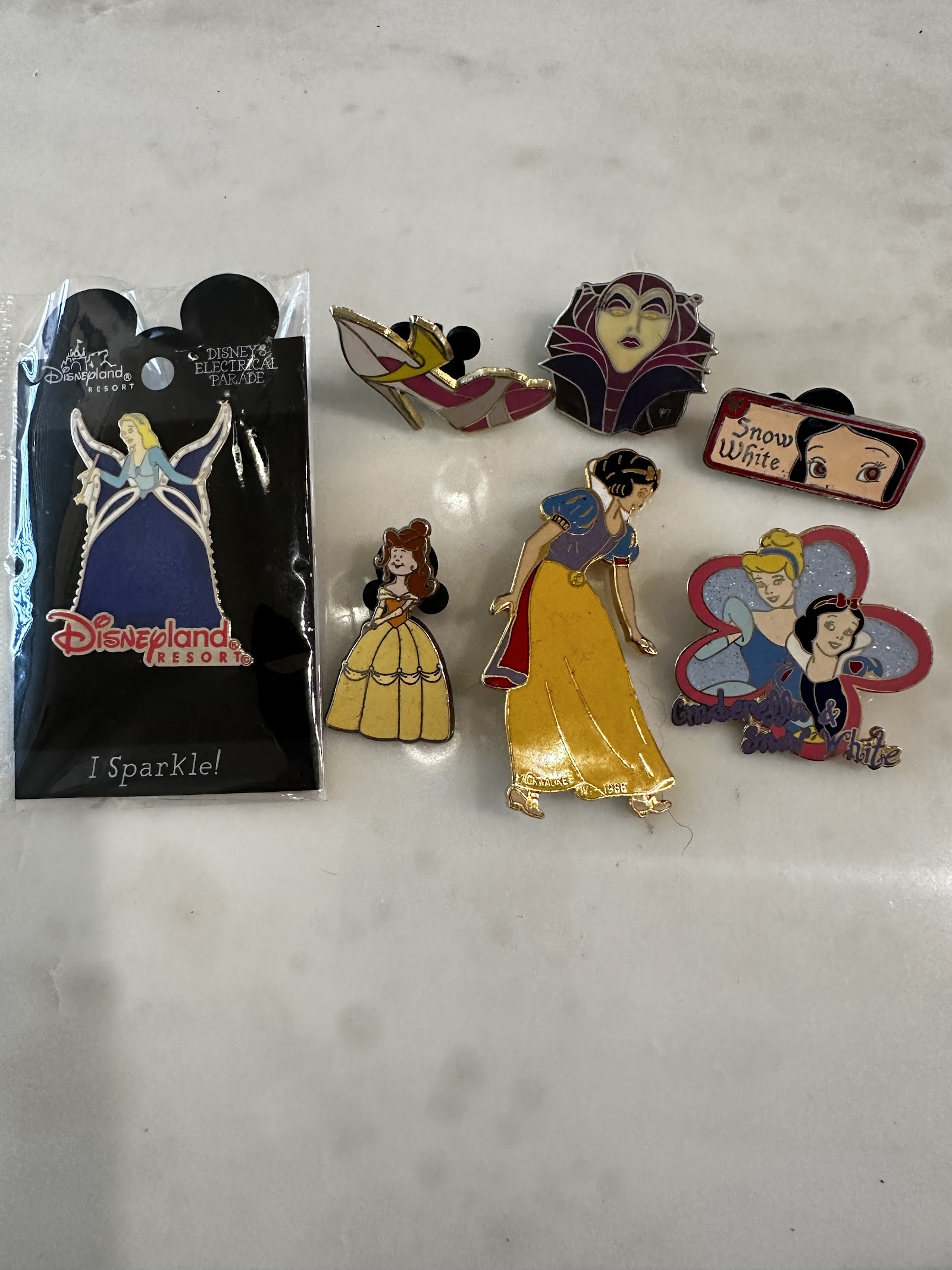 Seven Disney enamel pins including Snow White, Belle in yellow gown, Maleficent head, Evil Queen, and a packaged Main Street Electrical Parade Cinderella pin arranged together