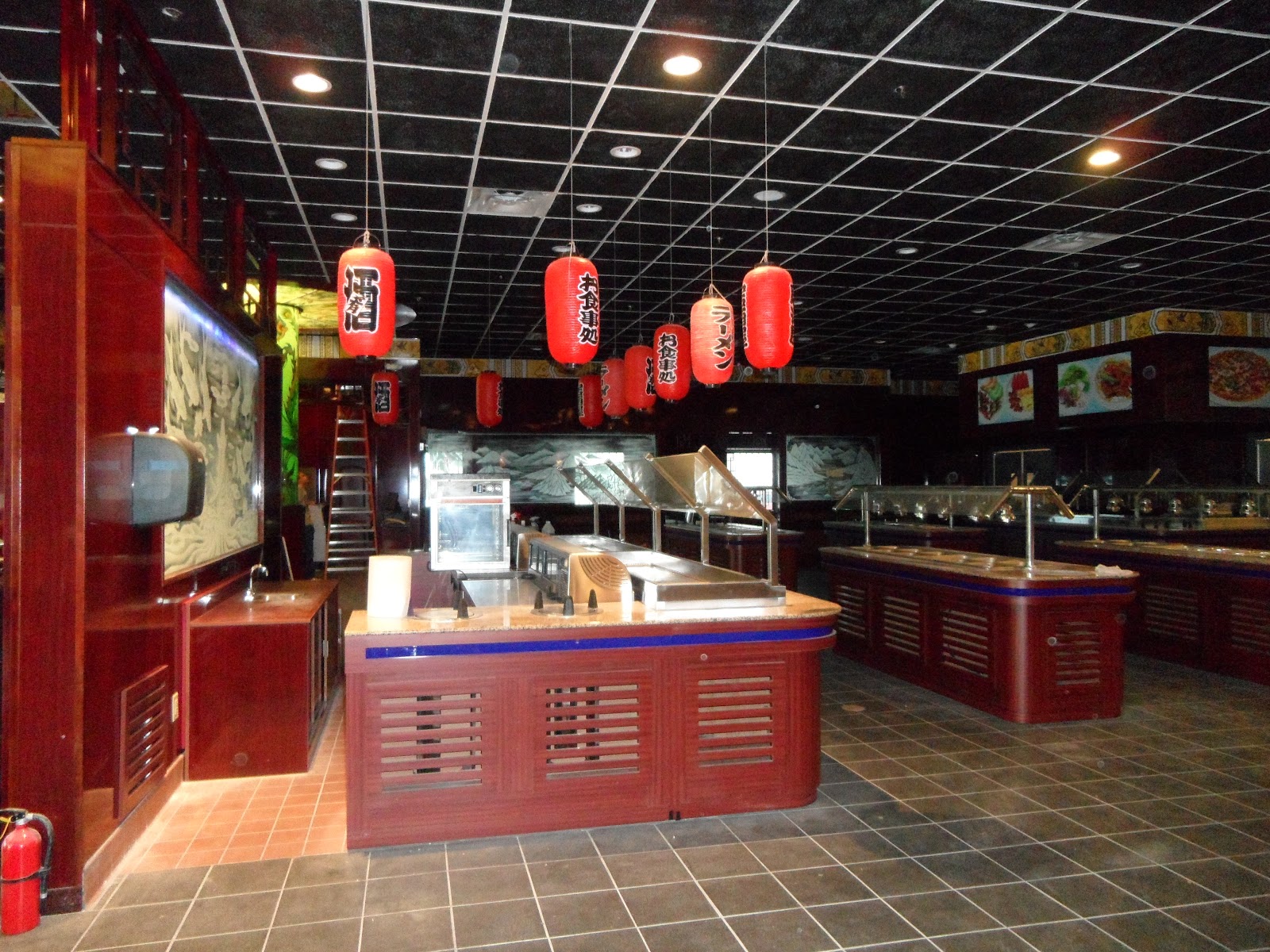 Restaurant interior with red lanterns hanging from a black grid ceiling, buffet stations with sneeze guards, and a wall mural.
