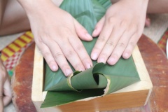 Lót 1 miếng lá dong lên bề mặt nếp. Nhẹ nhàng dùng tay gấp 2 bên lá dong lại như hình. Dùng dây lạt gói bánh chưng xanh lại cho cố định.