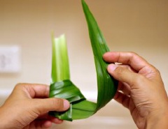 Lật úp lại, cài đầu lá dài vào trong 1 lần nữa, kéo cho chặt. Lúc này lá đã tạo thành 1 túi nhỏ rỗng bên trong.