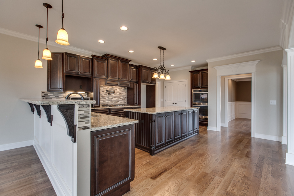 Kitchen interior with dark wood cabinetry, granite countertops, a central island, pendant lighting, and hardwood flooring.