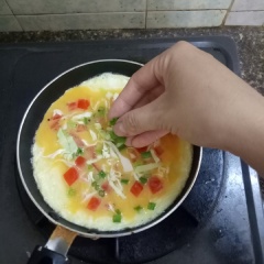 Đánh tan trứng gà với ít tiêu, muối. Đun nóng dầu ăn trong chảo, cho trứng vào chiên, dàn mỏng đều. Khi trứng chiên vẫn còn ướt mặt thì rắc thêm hành lá, cà chua lên đều mặt trứng. Đậy nắp chiên trứng chín đều là được.