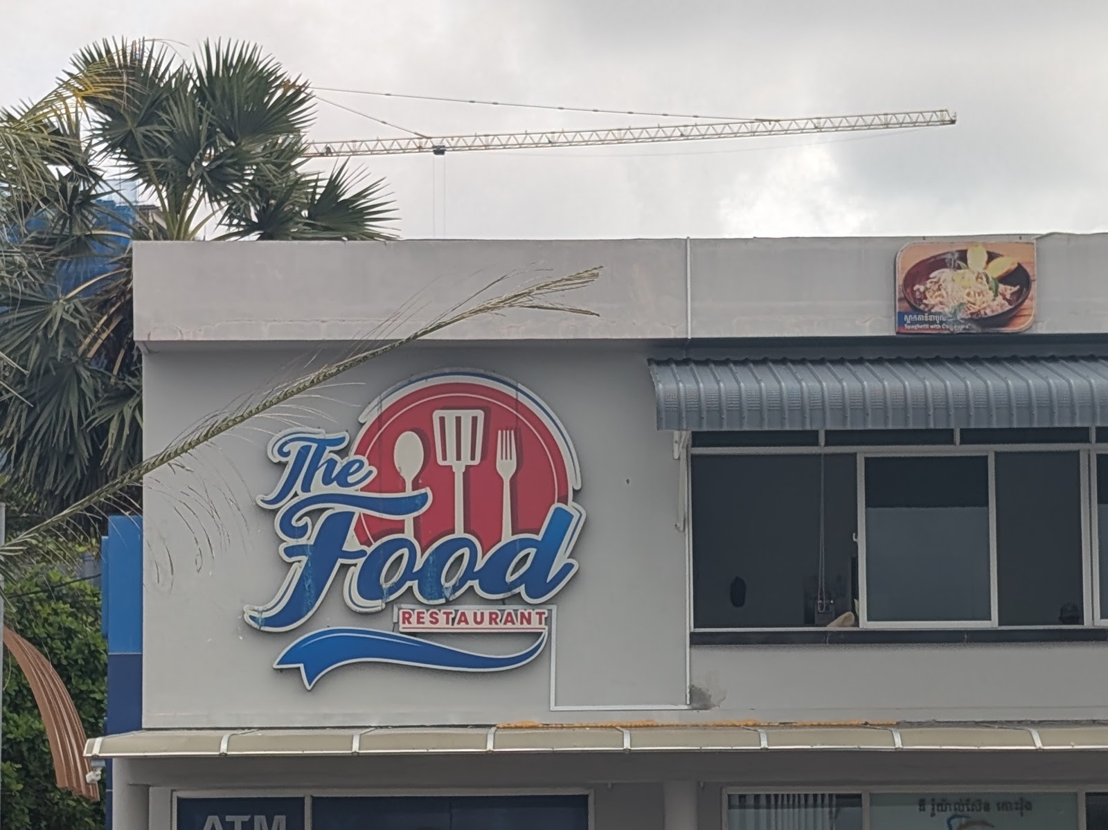 A photo of a side of a building among some trees with a sign
                 that says 'The Food Restaurant'