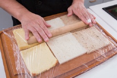 Cắt phần viền cứng xung quanh miếng sandwich rồi xếp từng lát ra mặt bàn hoặc thớt sạch. Phủ lớp nilon thực phẩm lên trên rồi dùng cây cán bột cán mỏng.