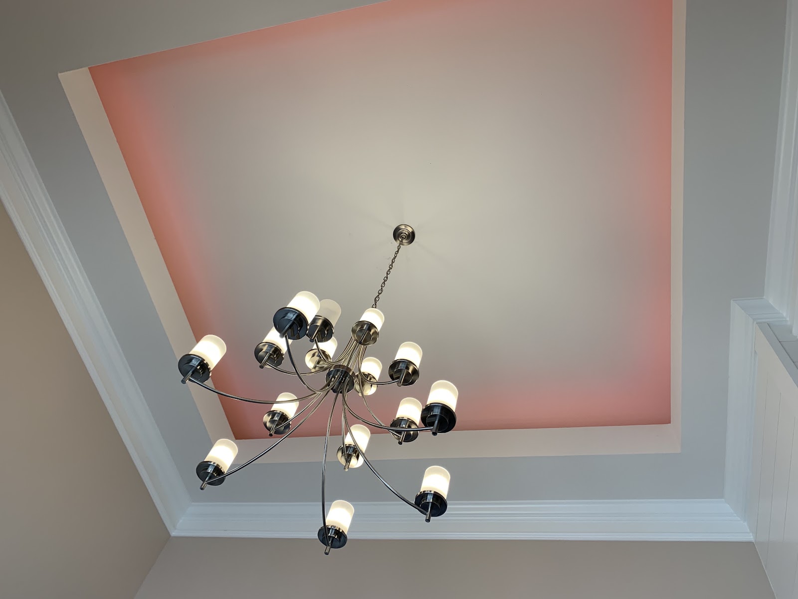 A multi-bulb chandelier hangs from a recessed ceiling featuring pink accent lighting and white crown molding.