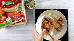 Cho vào chảo 2 muỗng canh dầu ăn, đổ tỏi vào phi thơm. Sau đó thêm xúc xích đã ướp vào xào chín. Tiếp tục cho cải chua, hành tím, ớt sừng vào, xào thêm 2 phút cho rau củ chín.