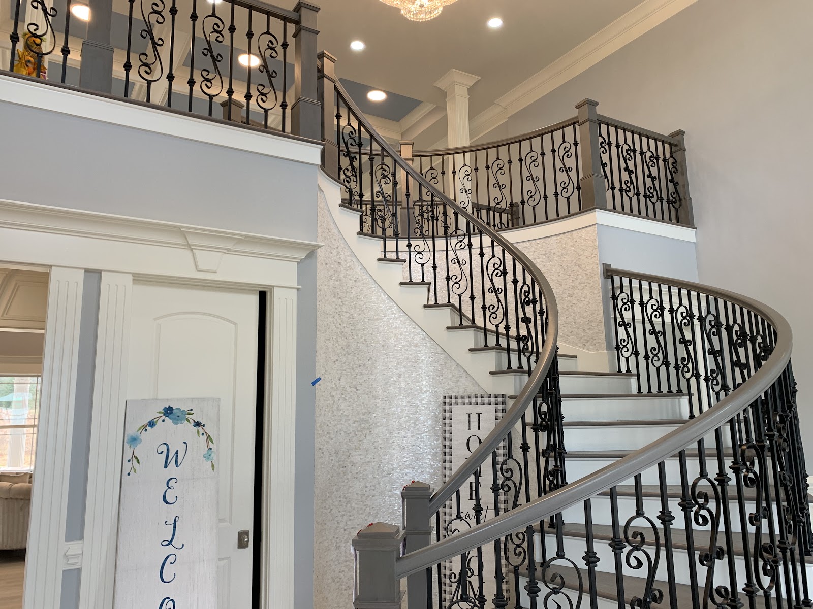 A curved staircase with dark metal scrollwork railings and light-colored treads leads to a second-floor landing in a home with light gray walls and white trim.