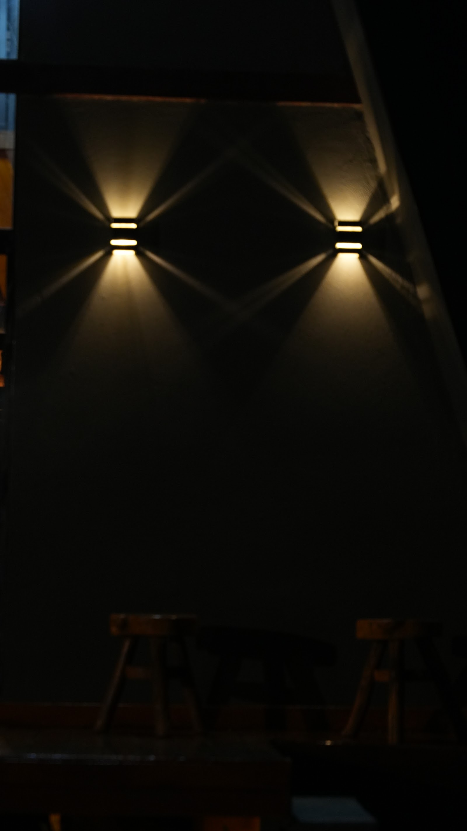 Detalhe real da iluminação externa embutida na fachada de madeira de um chalé Mei do Mato, à noite