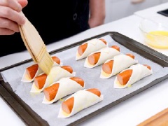 Đặt bánh cuộn xúc xích phô mai vào khay nướng, dùng cọ quét 1 lớp trứng lên trên. Bật lò nướng ở nhiệt độ 180 độ C, nướng bánh cuộn pho mát xúc xích trong lò khoảng 15 - 20 phút.