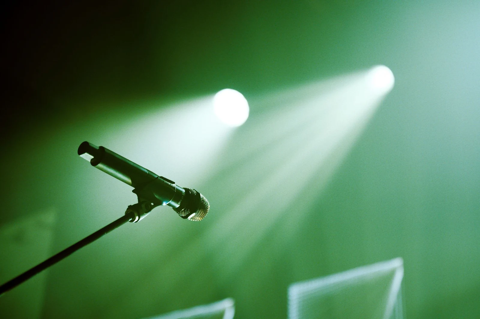 From below of black stand with microphone placed on stage with green illumination