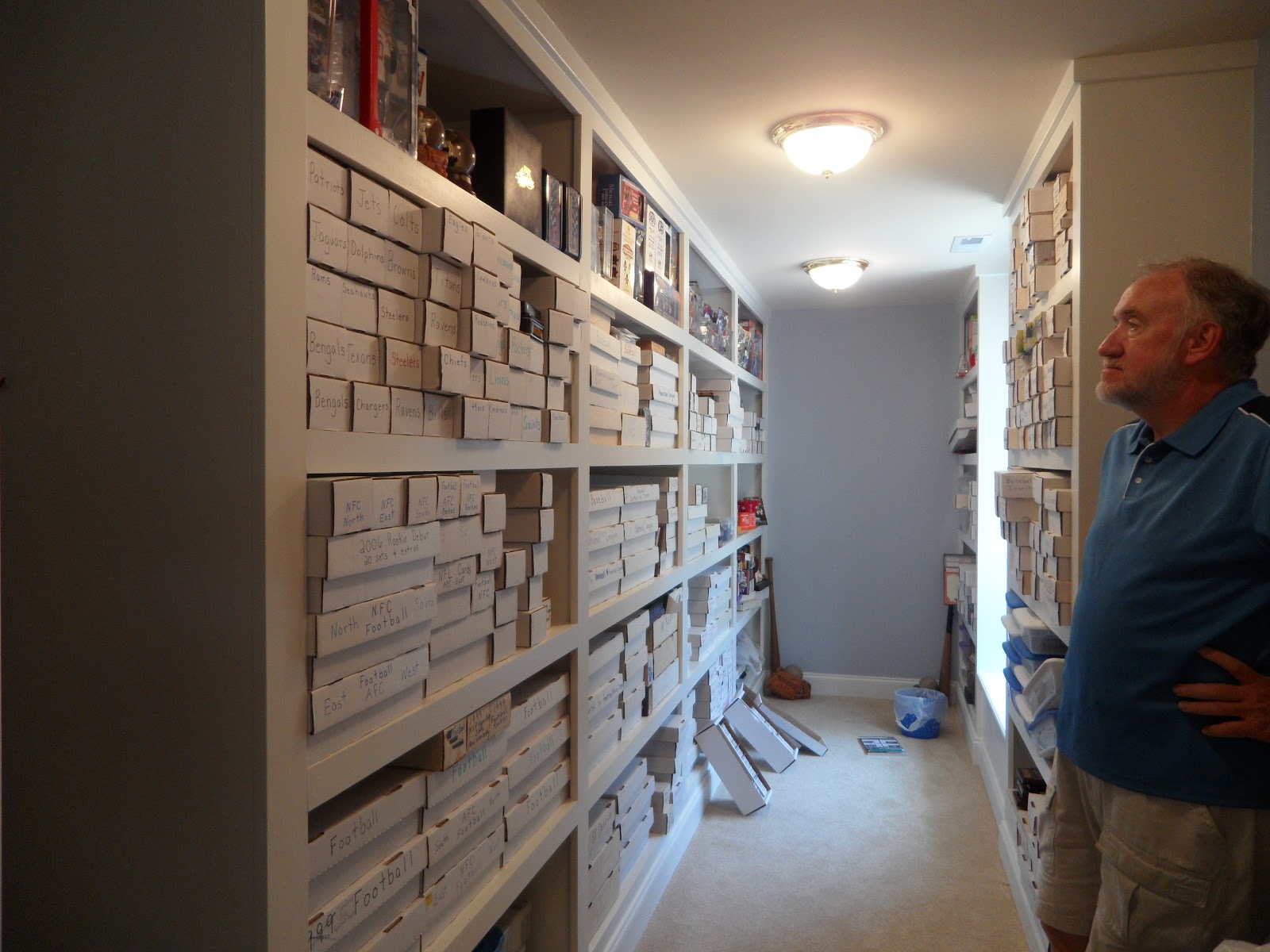 A man in a blue shirt stands in a narrow room lined with floor-to-ceiling white shelving units filled with white storage boxes.
