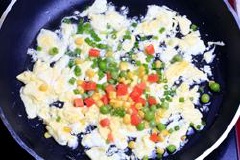 Chảo đặt lên bếp, đun nóng 1 muỗng canh dầu ăn, đổ trứng vào chảo, nhanh tay đảo cho trứng khỏi đông bánh lại. Tiếp đó cho đậu Hà Lan, cà rốt, bắp hột đảo nhanh tay. Nêm thêm chút gia vị cho đậm đà.  