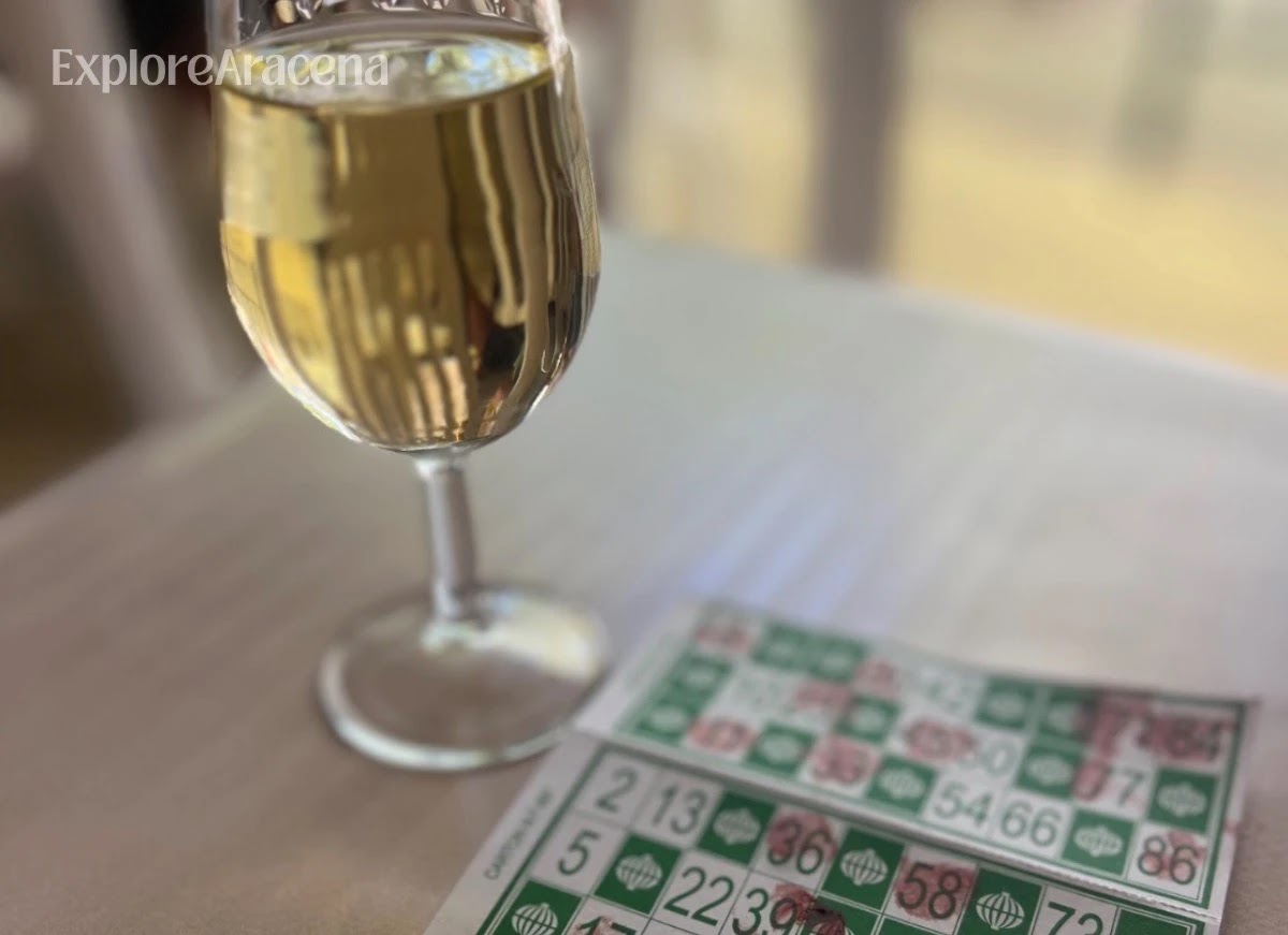 Glass of white wine beside a bingo card on a caseta table at the Feria de Aracena.