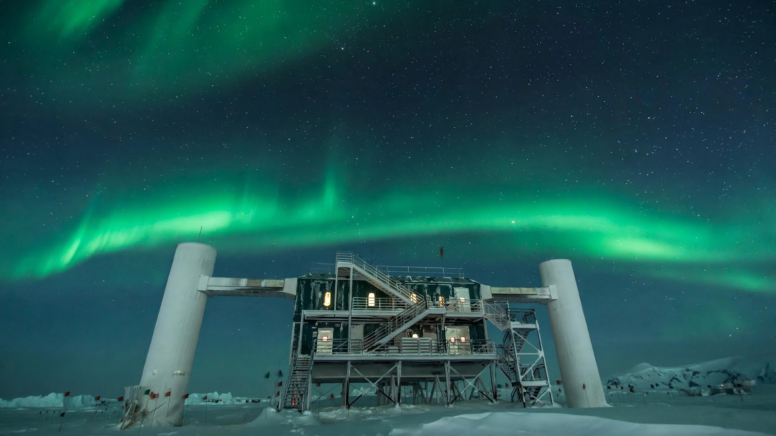 The IceCube Laboratory building at the South Pole under a starry sky with green aurora