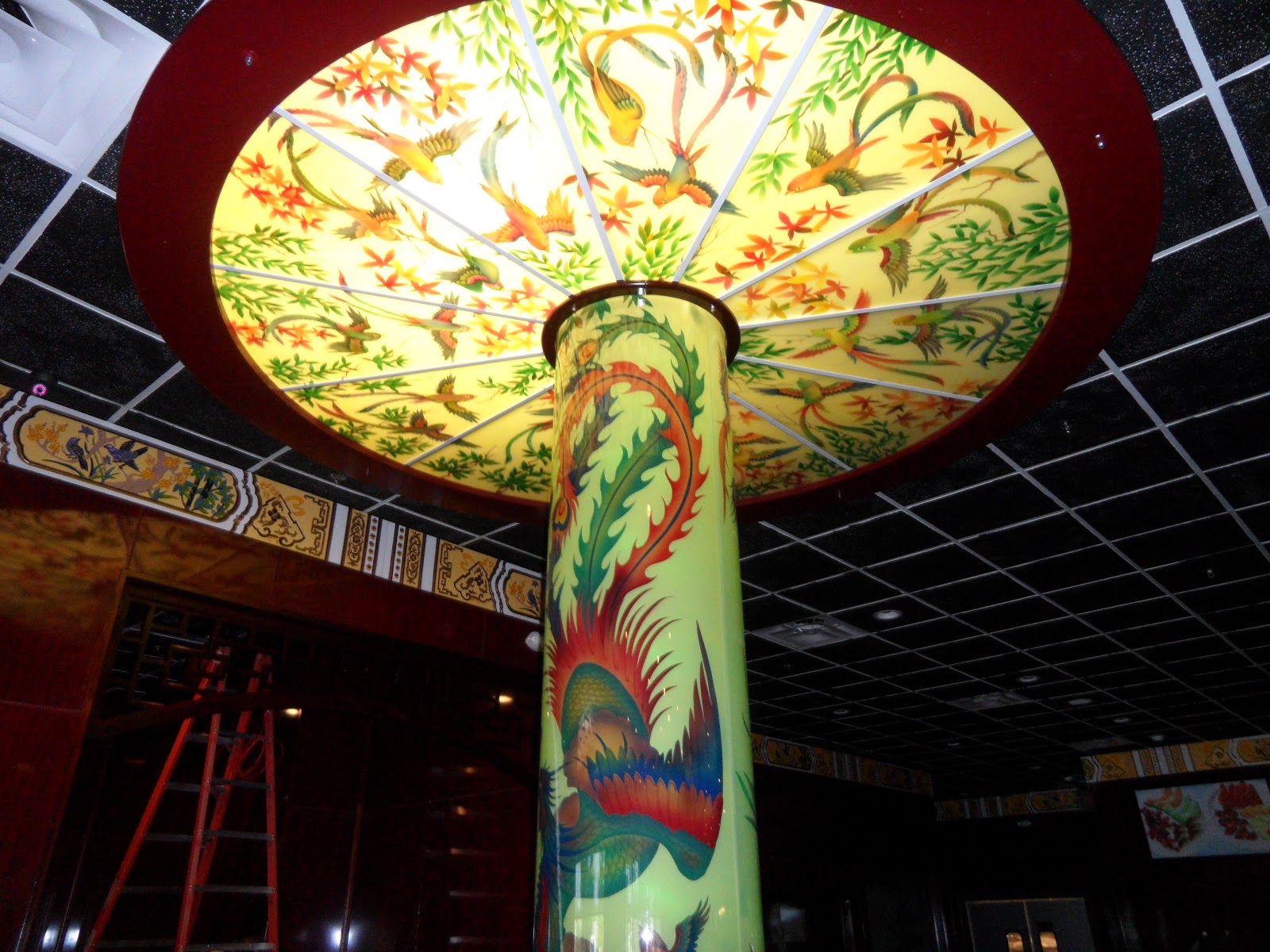 A decorative column with bird and floral illustrations, supporting a large circular light fixture with matching artwork on a black grid ceiling.