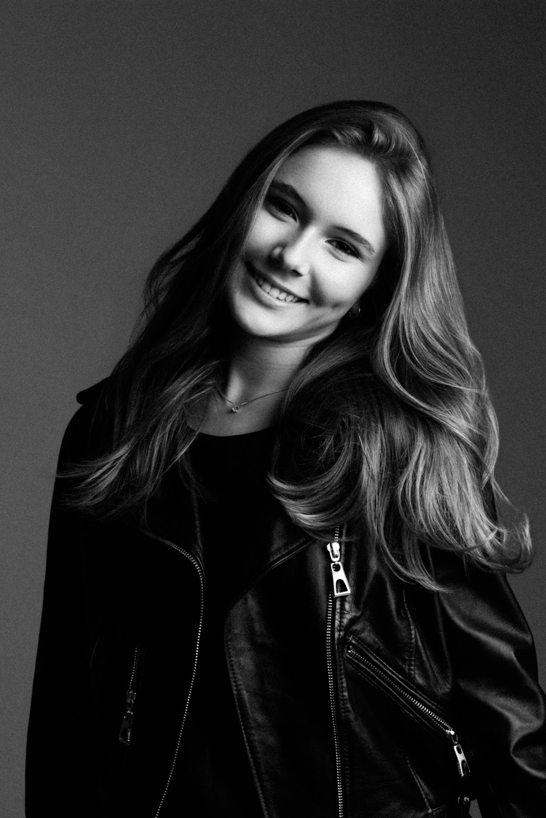 Maria Luiza sorrindo em retrato preto e branco com cabelos soltos e fundo neutro.