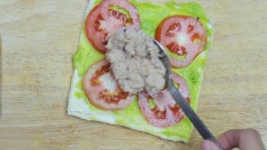 Phết bơ đều lên miếng sandwich. Xếp cà chua rồi đến cá ngừ sao cho chừa khoảng 1cm ở mép để dễ cuốn.