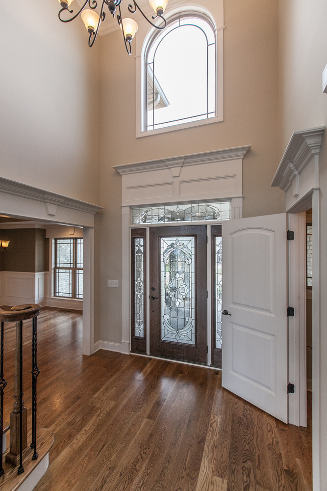 Entryway with hardwood floors, a dark wood front door with decorative glass, and a large arched window above.