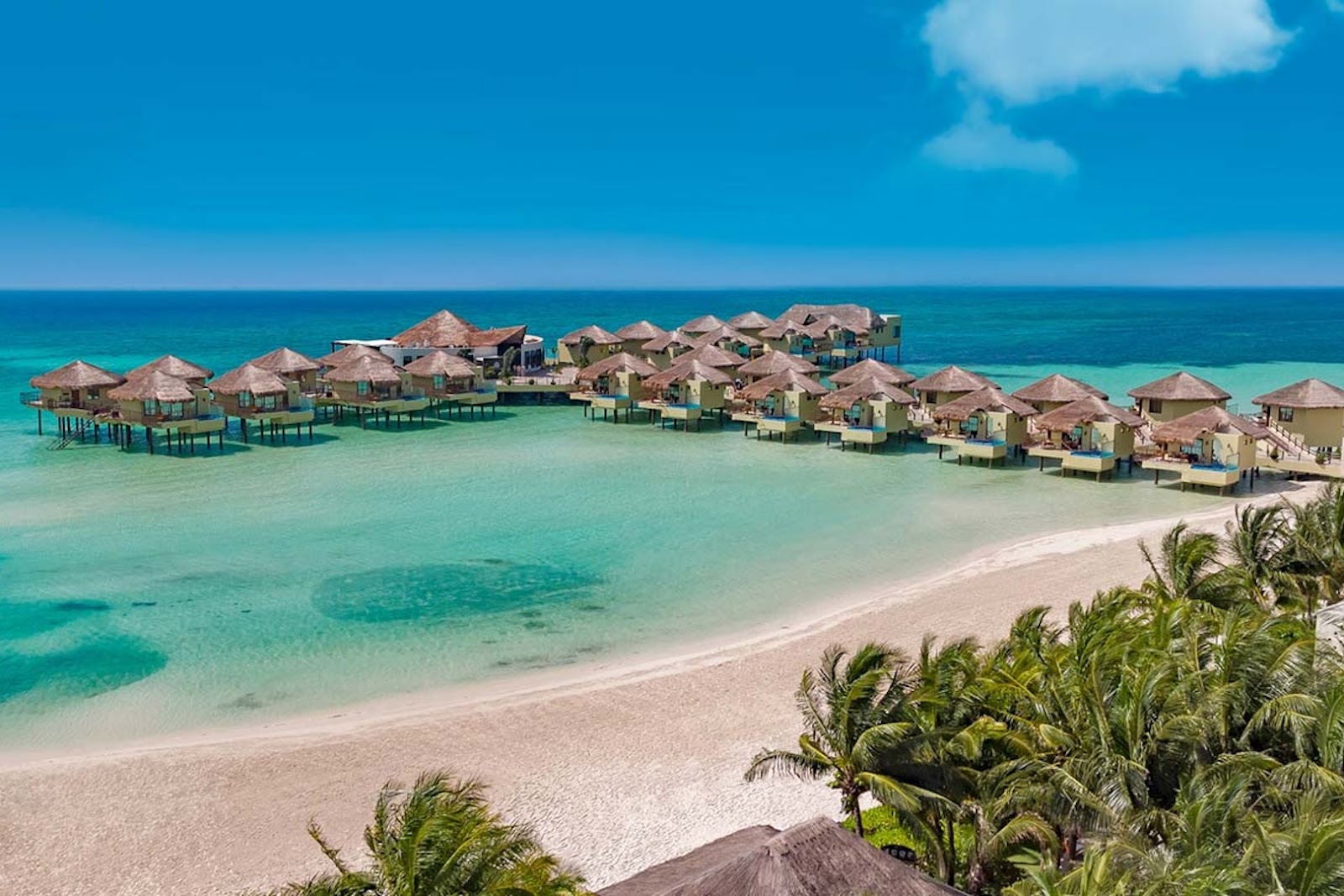 Palafitos overwater bungalows at El Dorado Maroma extending over turquoise Caribbean water in Mexico’s Riviera Maya.