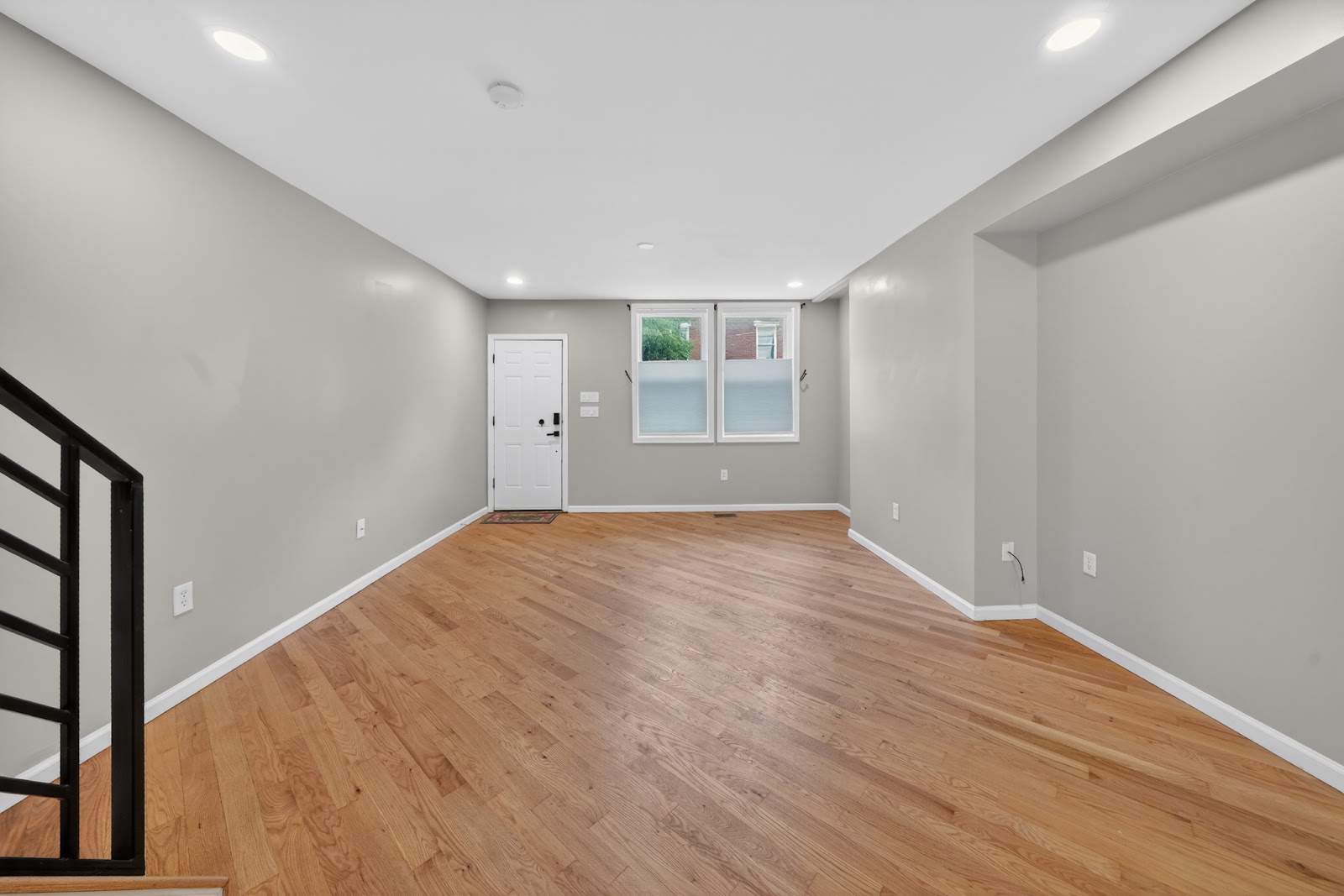 Renovated open-plan living room with fresh gray walls, new hardwood floors, recessed lighting, and modern black stair railing — HousePro South Jersey whole-home renovation