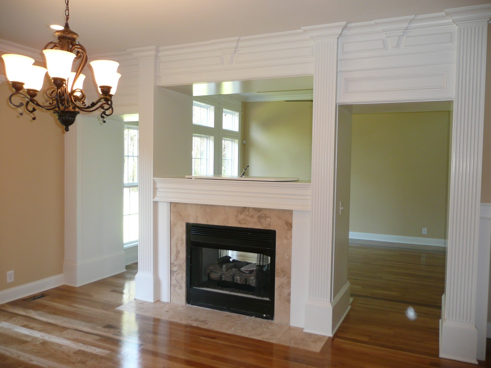 Interior view of a room with hardwood floors, a fireplace featuring a stone surround and white mantel, and an ornate white-trimmed doorway.
