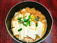 Cho thịt ba chỉ vào nồi cùng với 300g kim chi, 1 muỗng cà phê bột ớt, tỏi băm, gừng băm rồi bật bếp xào sơ qua cho thịt chín sau đó thêm nước nấu cho sôi. Tiếp theo bạn thêm nước kim chi vào nấu cùng cho sôi lên, để lửa nhỏ nấu thêm 15 phút thì cho đậu hũ vào, đun khoảng vài phút nữa thì cho hành lá rồi tắt bếp, rắc thêm chút muối và tiêu cho dậy mùi thơm và múc canh kim chi đậu hũ non ra tô để thưởng thức.