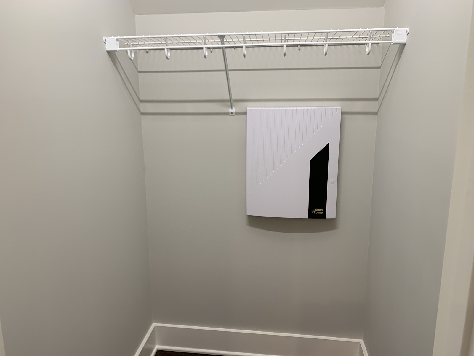 A small interior space with neutral walls, a white wire shelf, and a white rectangular utility panel mounted on the wall.