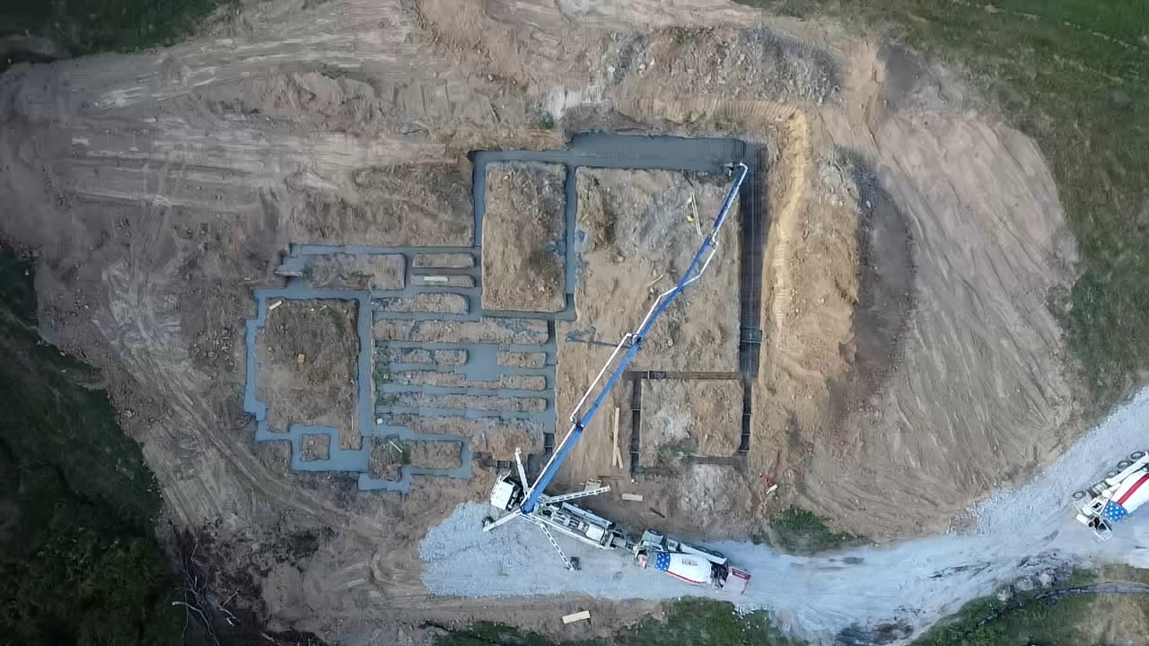 Top-down aerial view of a concrete pump truck pouring foundation footings for a new building on an excavated site.