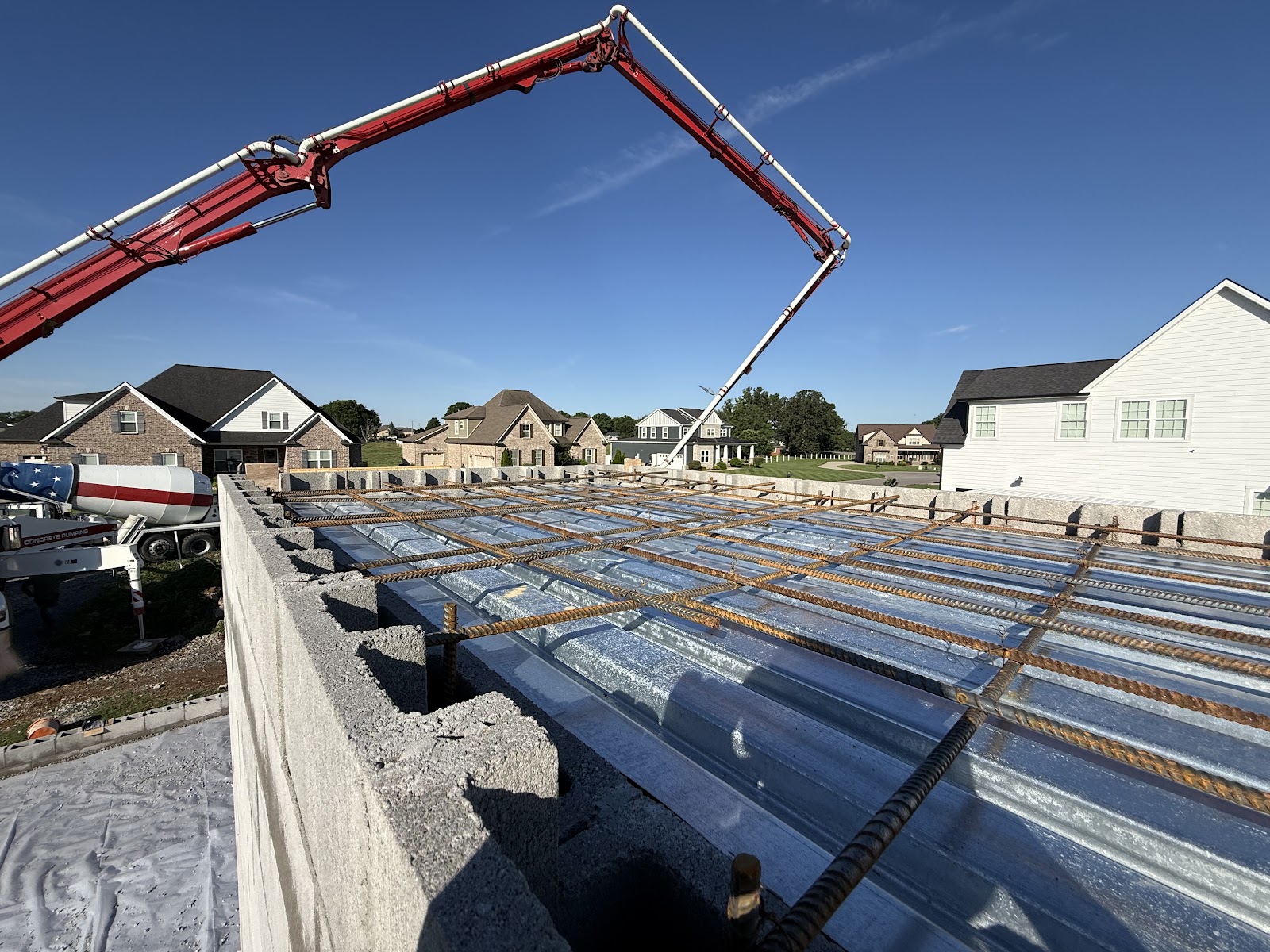 View from the top of a storm shelter under construction, showing corrugated metal decking and a rebar grid with a concrete pump arm overhead.