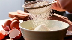 Rây 75gr bột mì số 8 và 1 muỗng cà phê bột nở vào tô trứng rồi dùng phới dẹt trộn đều từ ngoài vào trong.