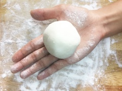 Tiến hành chia bột thành các phần bằng nhau, mỗi phần có khối lượng 50gr. Cũng dùng màng bọc thực phẩm đậy lại phần bột chưa làm để bột không bị khô. Sau đó lấy một miếng bột cho ra mặt phẳng, dùng lòng bàn tay ép dẹt miếng bột, nặn thành hình tròn, rìa ngoài mỏng hơn ở giữa. Sau đó lấy một phần nhân đã làm ở trên đặt vào giữa miếng bột, gói lại.