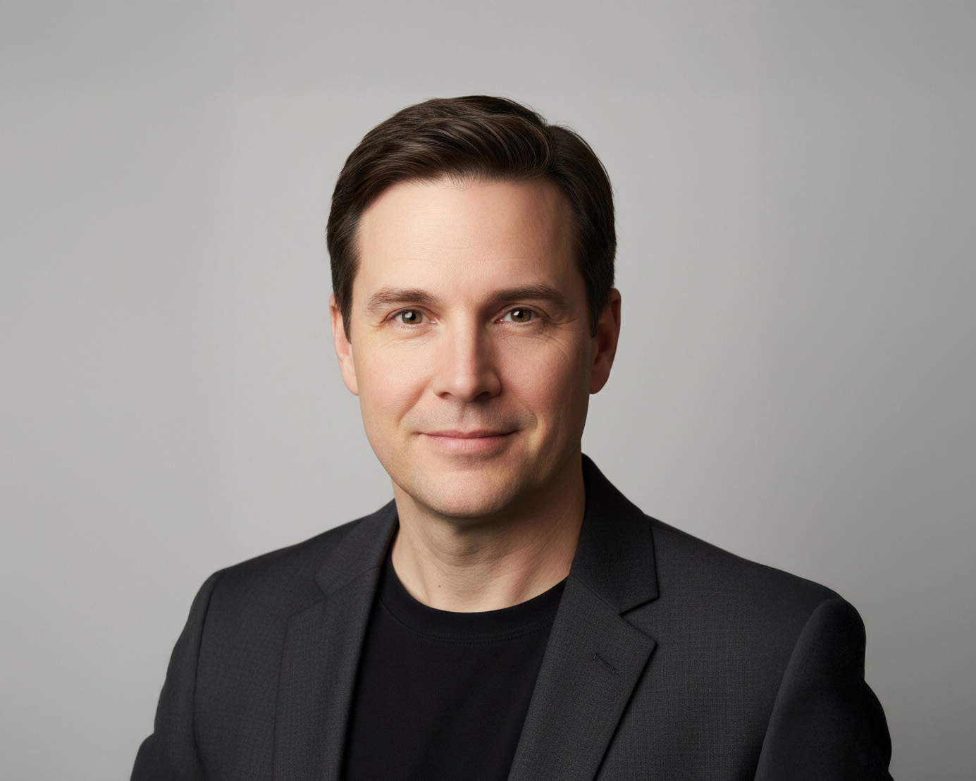 Executive headshot of a man in a charcoal blazer and black shirt, clean modern background and natural expression.