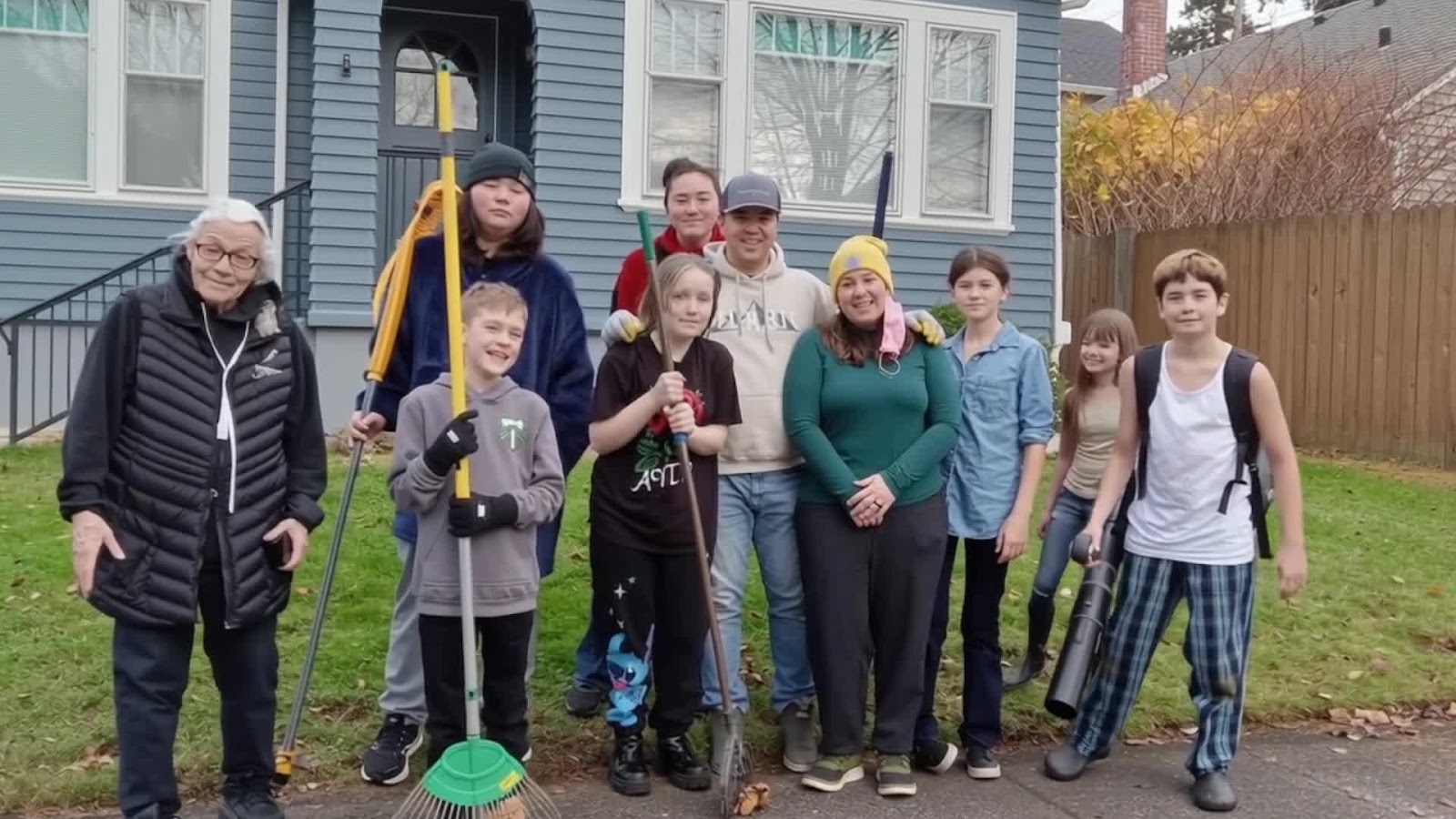 Leaf of Joy volunteers of different ages standing together outside a house with rakes and yard tools.