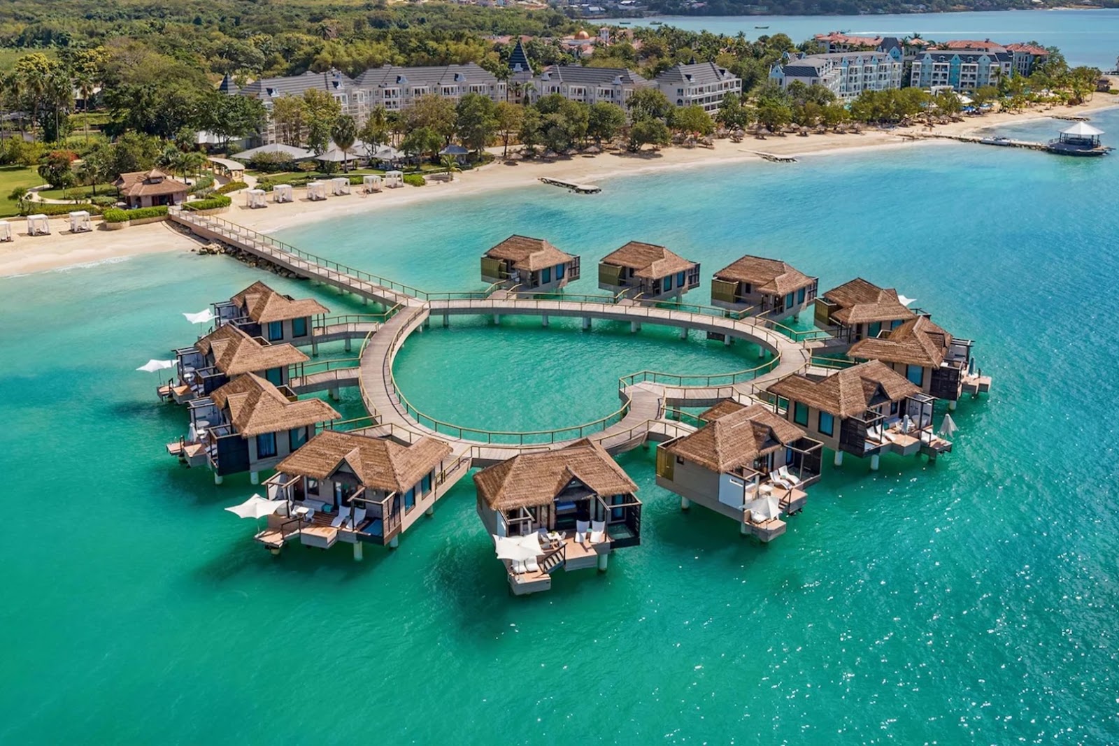 Overwater bungalows at Sandals South Coast in Jamaica arranged above clear Caribbean water.