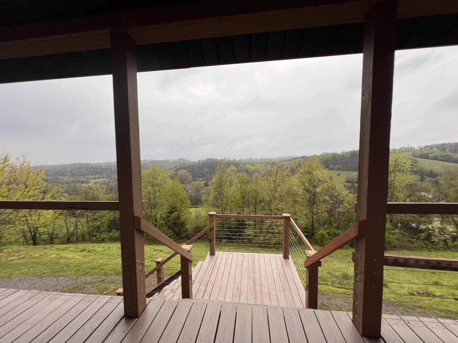 View from a wooden deck with wire railings overlooking a scenic rural landscape of green hills and trees.