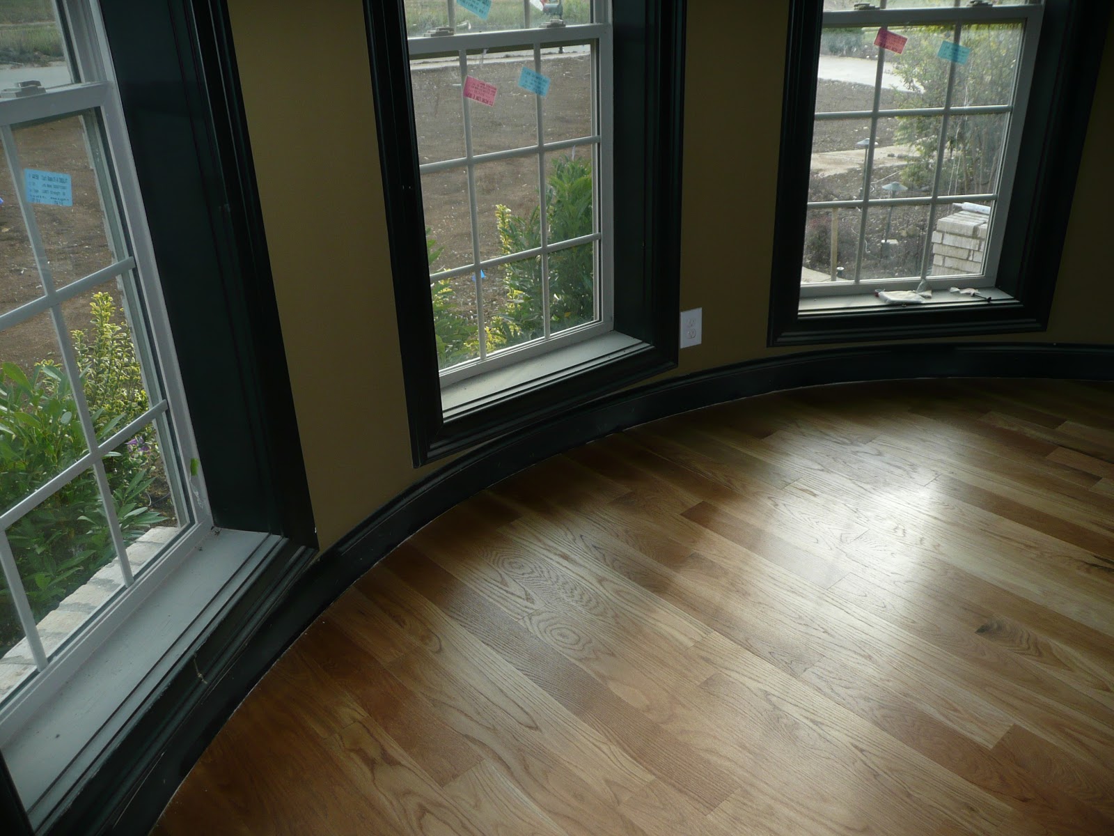 A curved wall with three windows, dark baseboards, and hardwood flooring.