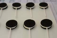 Tách bánh Oreo, cho một ít chocolate chảy và giữa bánh rồi đặt ngay que kẹo vào. Chocolate sẽ có tác dụng cố định que kẹo vào bánh. Kẹp bánh trở lại. Ấn nhẹ để hai lớp bánh dính chặt với nhau. Để bánh trên khay trong 10-15 phút để chocolate cứng lại.
