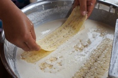 Cho chuối vào hỗn hợp bột mì, dùng đũa gạt để cho bột mì không bị vón lại trên chuối vừa cán.