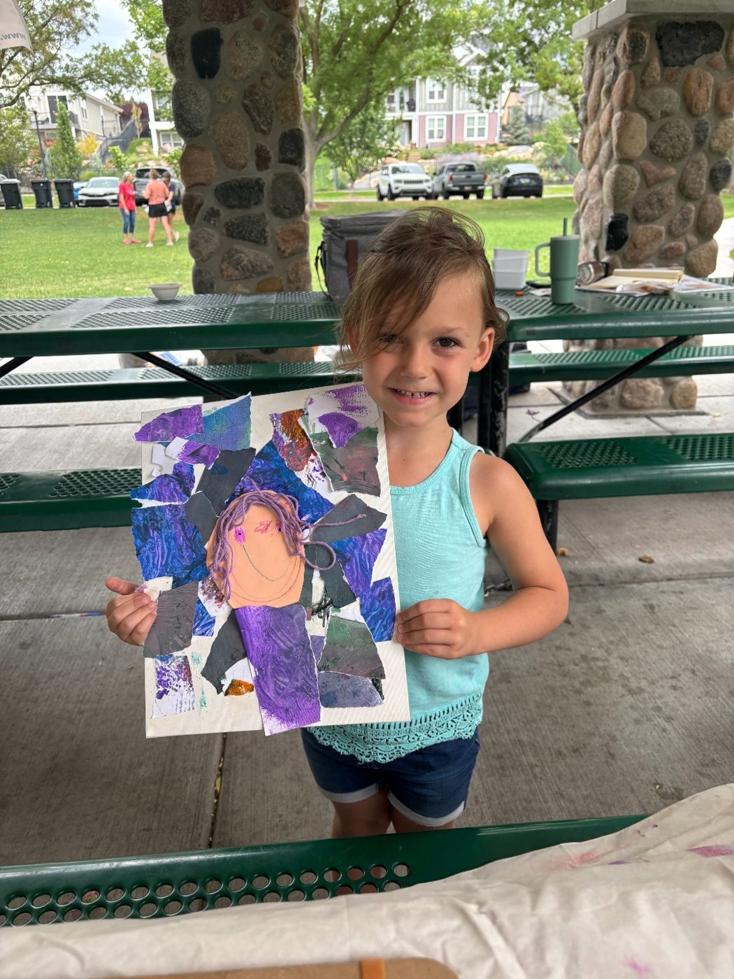 A smiling young artist proudly holding up her finished torn-paper collage self-portrait