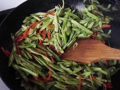 Đun nóng 2 muỗng canh dầu ăn, cho ớt đã cắt vào đảo đều tay cho thơm. Sau đó, cho đậu que vào, nêm ít muối, hạt nêm, chút nước vào, xào cho đậu que chín mềm là được.
