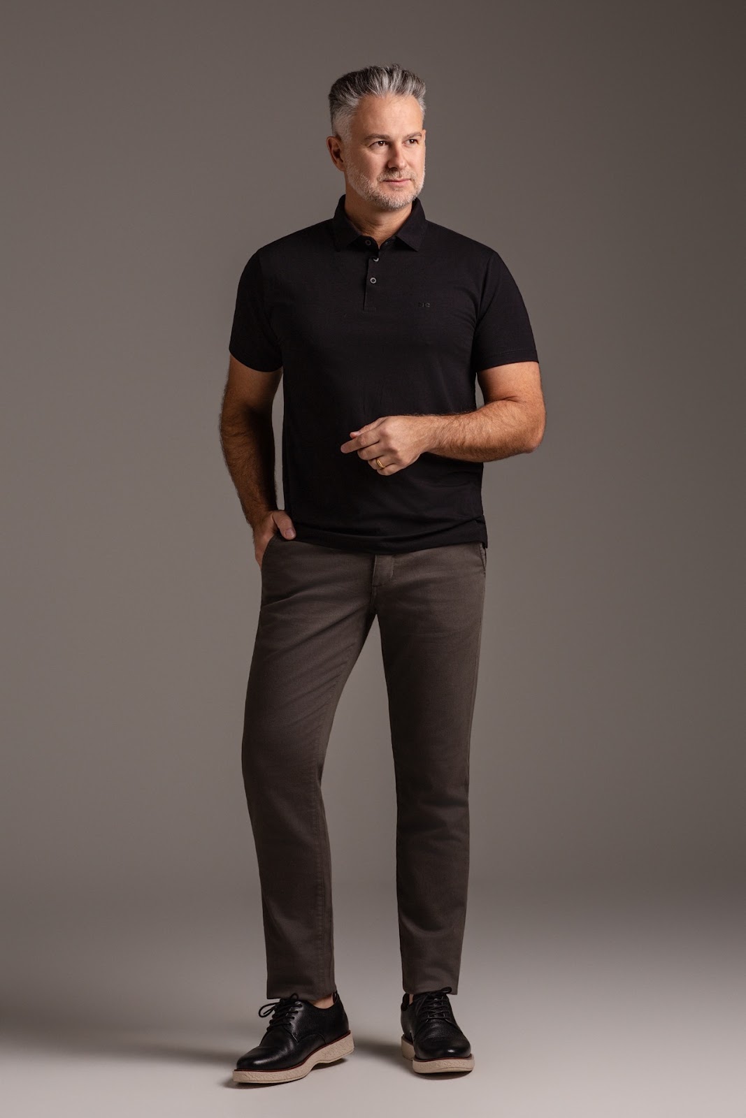 Retrato masculino com polo preta e cal�a neutra em fundo de est�dio.