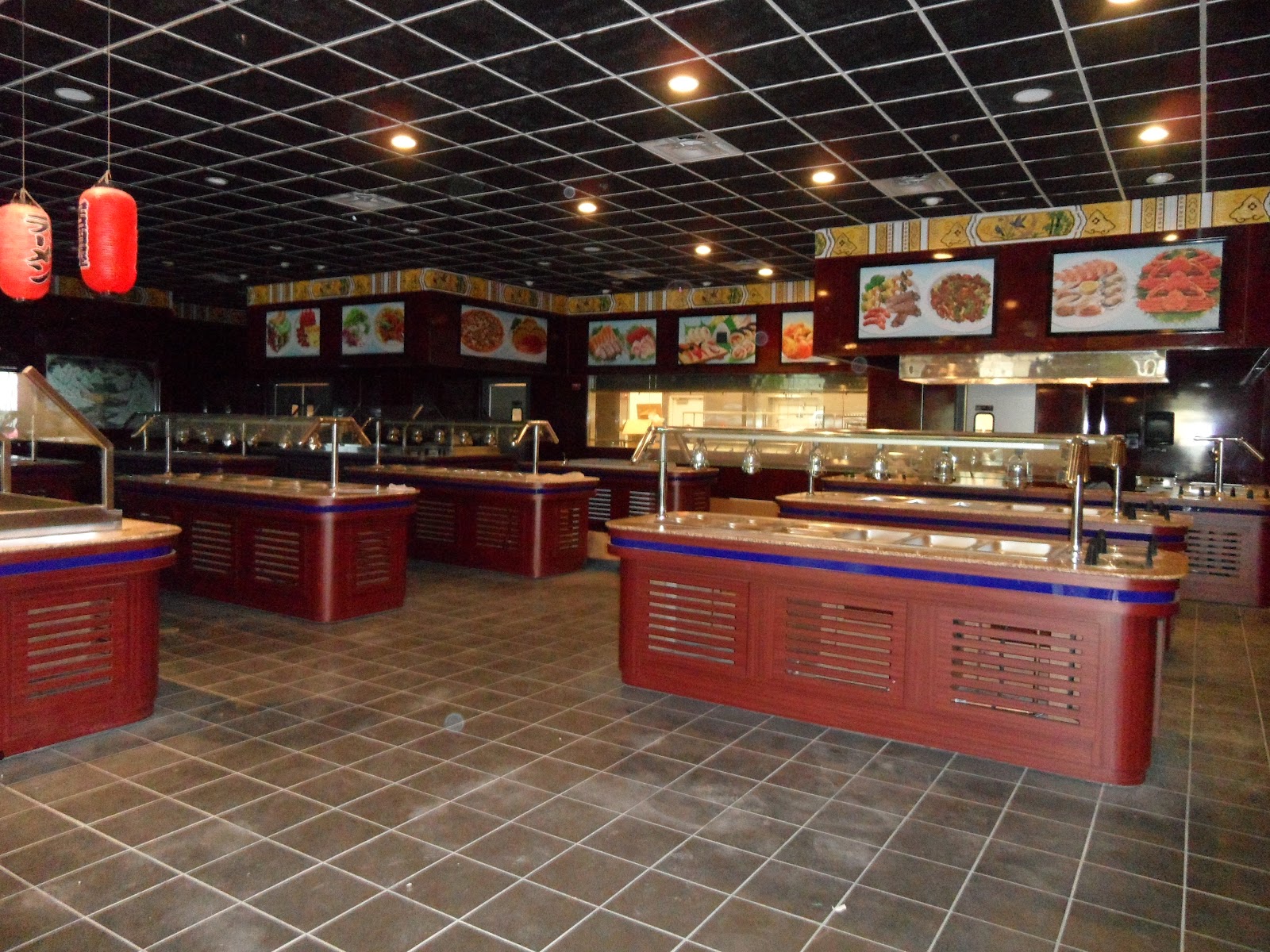 Interior view of a restaurant buffet area featuring multiple red serving stations with sneeze guards, a tiled floor, and a black grid ceiling with recessed lighting.