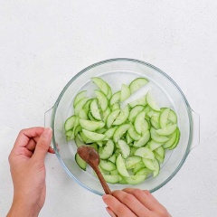 Làm dưa leo muối chua: Lấy 1 trái dưa leo cắt lát cho vào tô cùng 1/2 muỗng cà phê muối, 1/2 muỗng cà phê đường và 1 muỗng canh giấm táo, trộn đều và để sang một bên.
