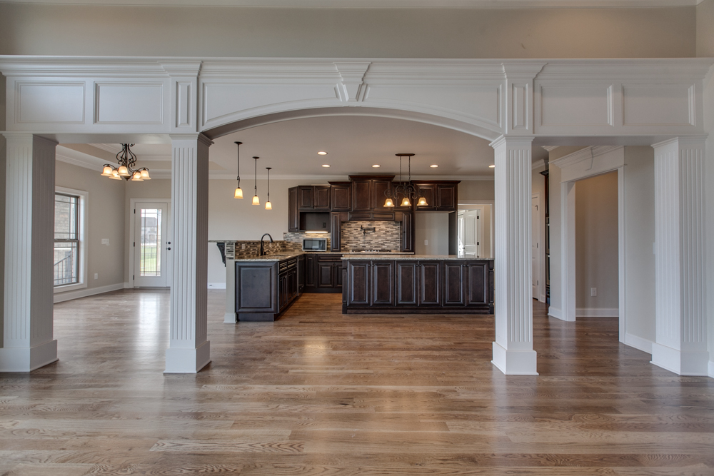 View through a white decorative archway into a kitchen with dark wood cabinets, a center island, and hardwood flooring.
