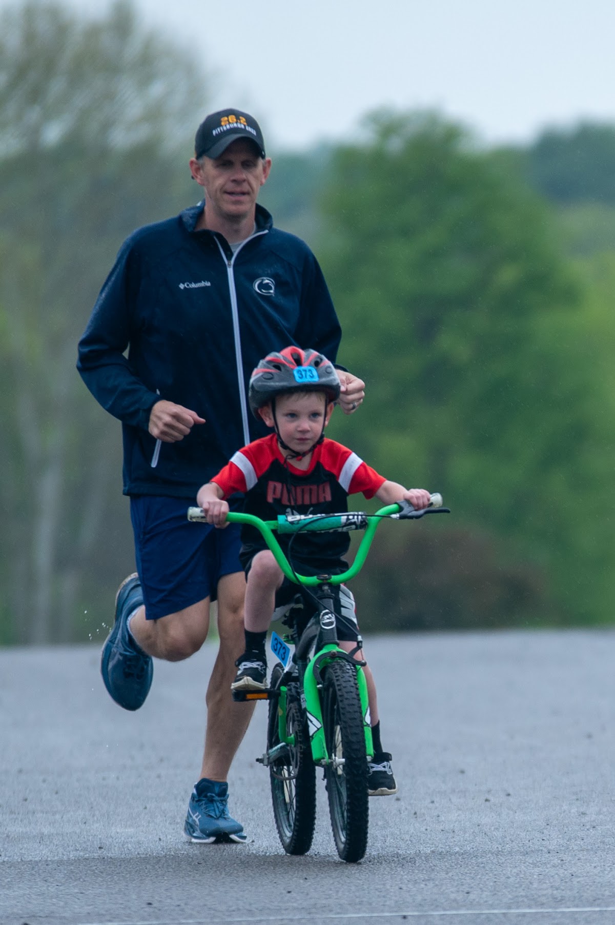 A small child riding at the Mighty Moraine youth race, with an adult running alongside