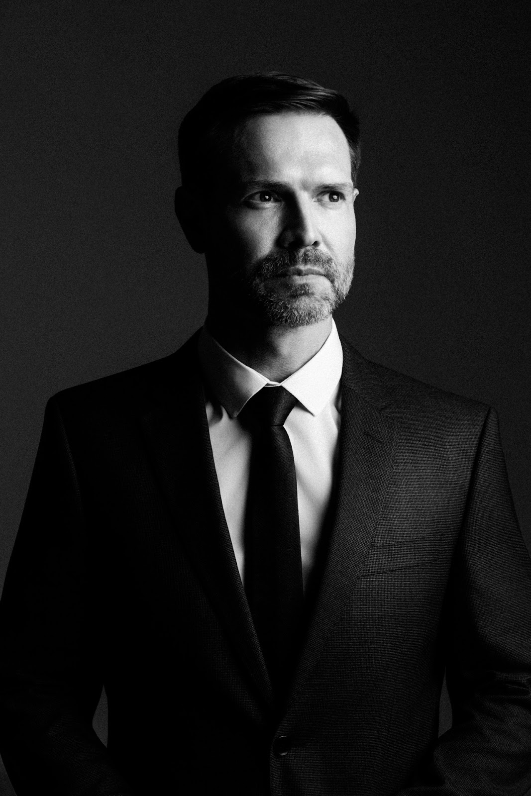 Retrato corporativo dram�tico em preto e branco com terno e gravata em fundo escuro.