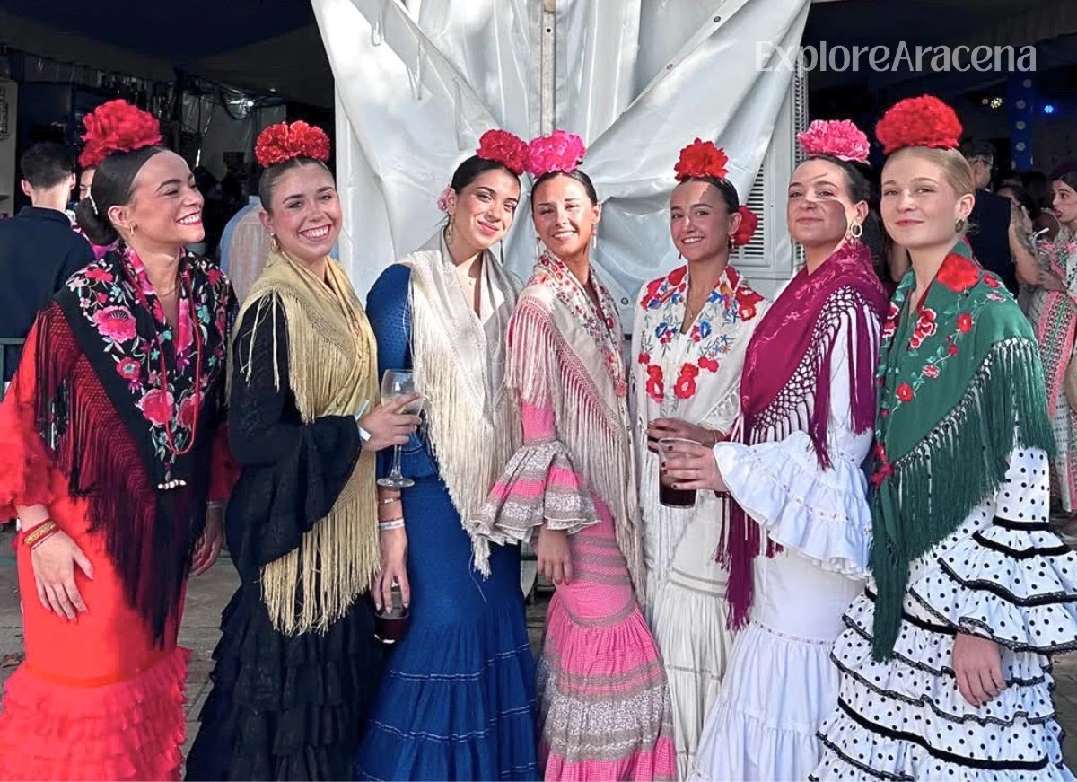 Seven young women posing together in colourful feria dresses at the Feria de Aracena.