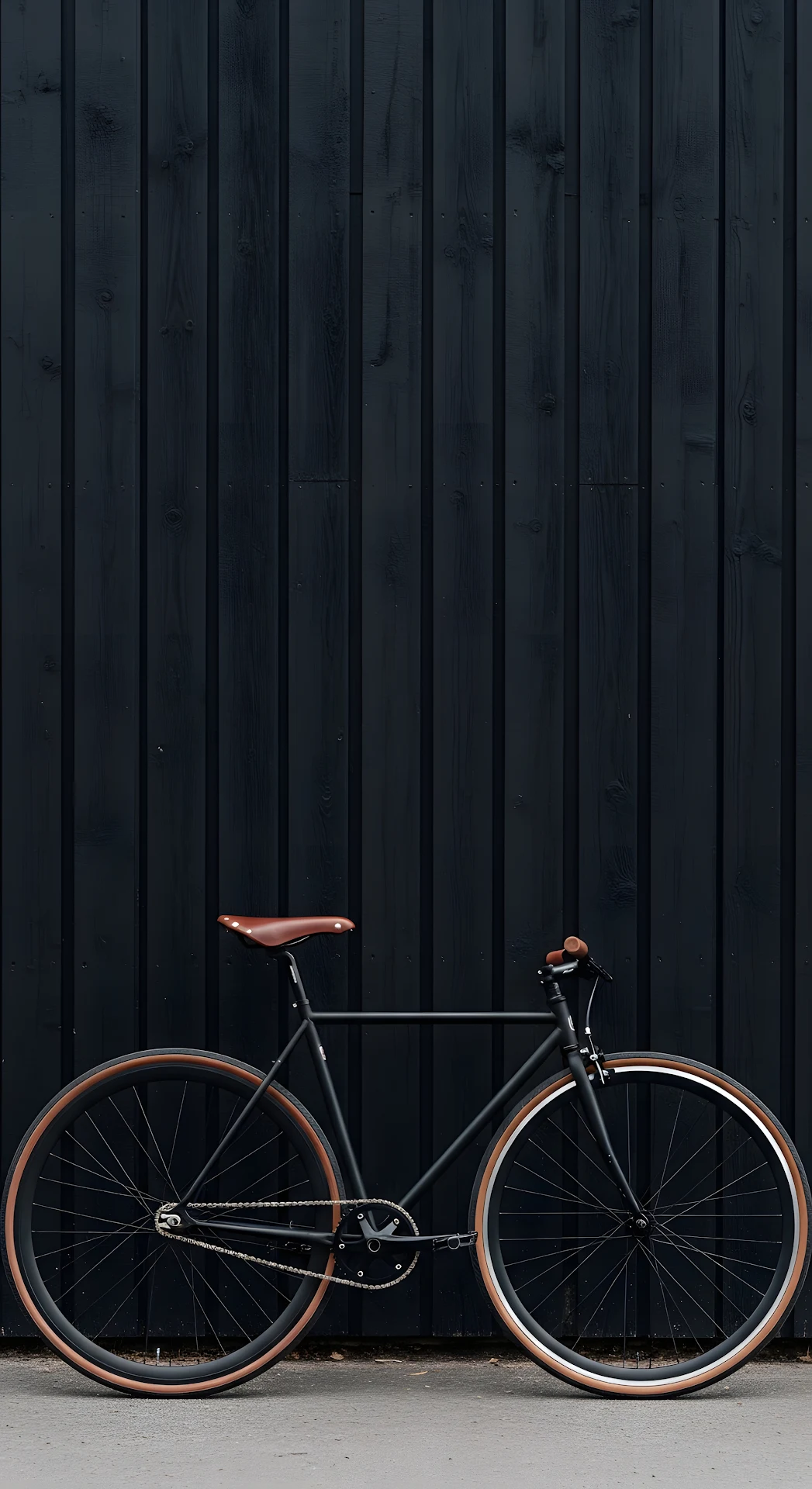 Minimalist Black Single-Speed Bicycle with Brown Tires Against Dark Textured Wall - Free 4K mobile Wallpaper